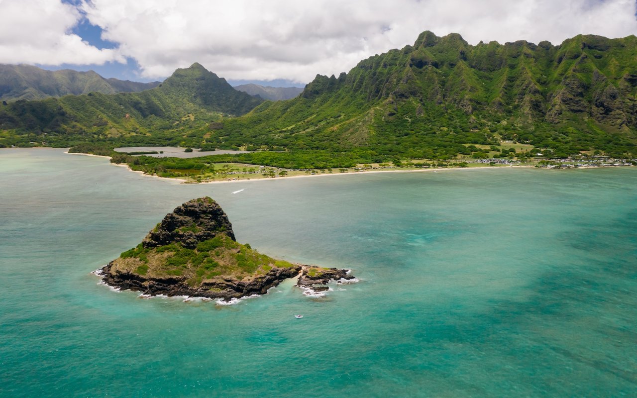 Kualoa Beach and turquoise bay, with a rocky islet and lush green mountains.