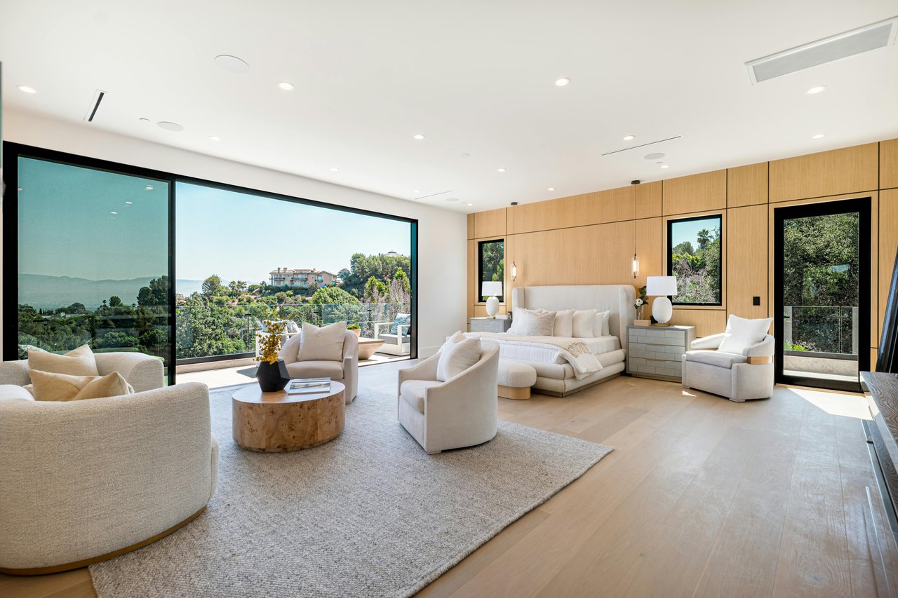 Spacious modern luxury master bedroom with panoramic mountain and ocean views, featuring large glass doors and contemporary decor, perfect for upscale real estate buyers.