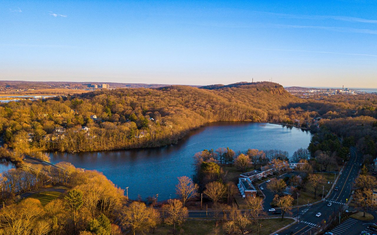 Aerial view of a lake amid autumn woods and homes, with a rocky hill in the distance.