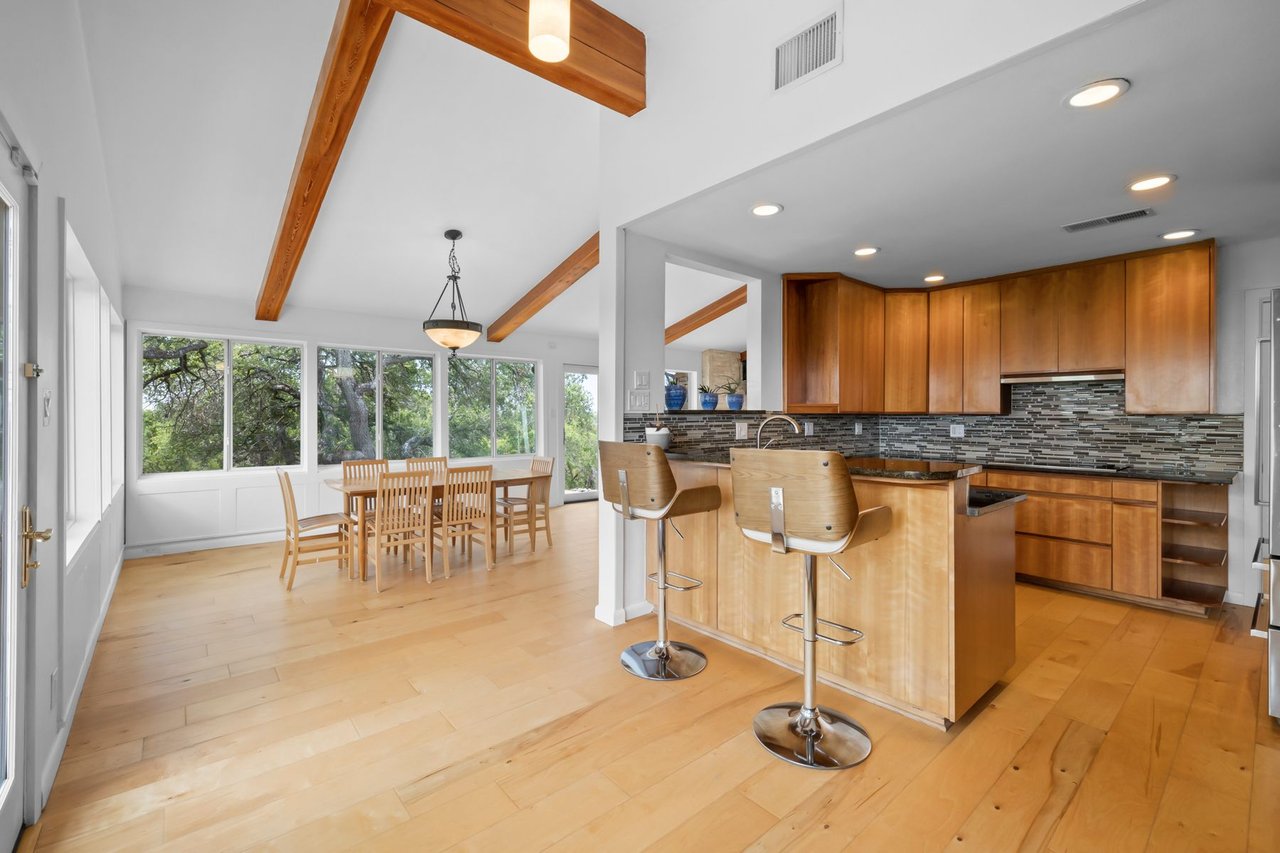 Great room with a wood-beamed vaulted ceiling, wall of windows, and open kitchen island at 3935 Lago Vista Drive, a hilltop Mid-Century Modern home near Lake Travis in Austin, TX.