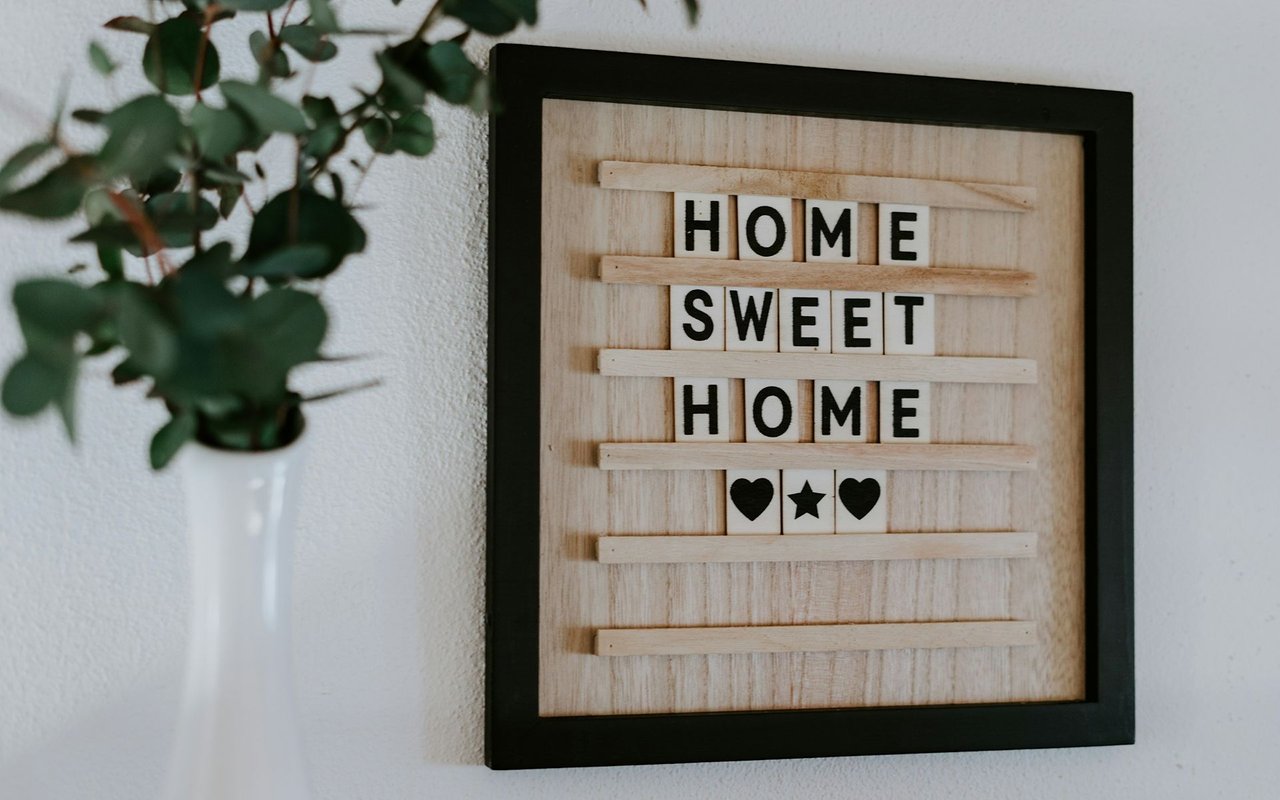 Framed wooden “Home Sweet Home” sign with heart and star tiles beside a leafy plant.