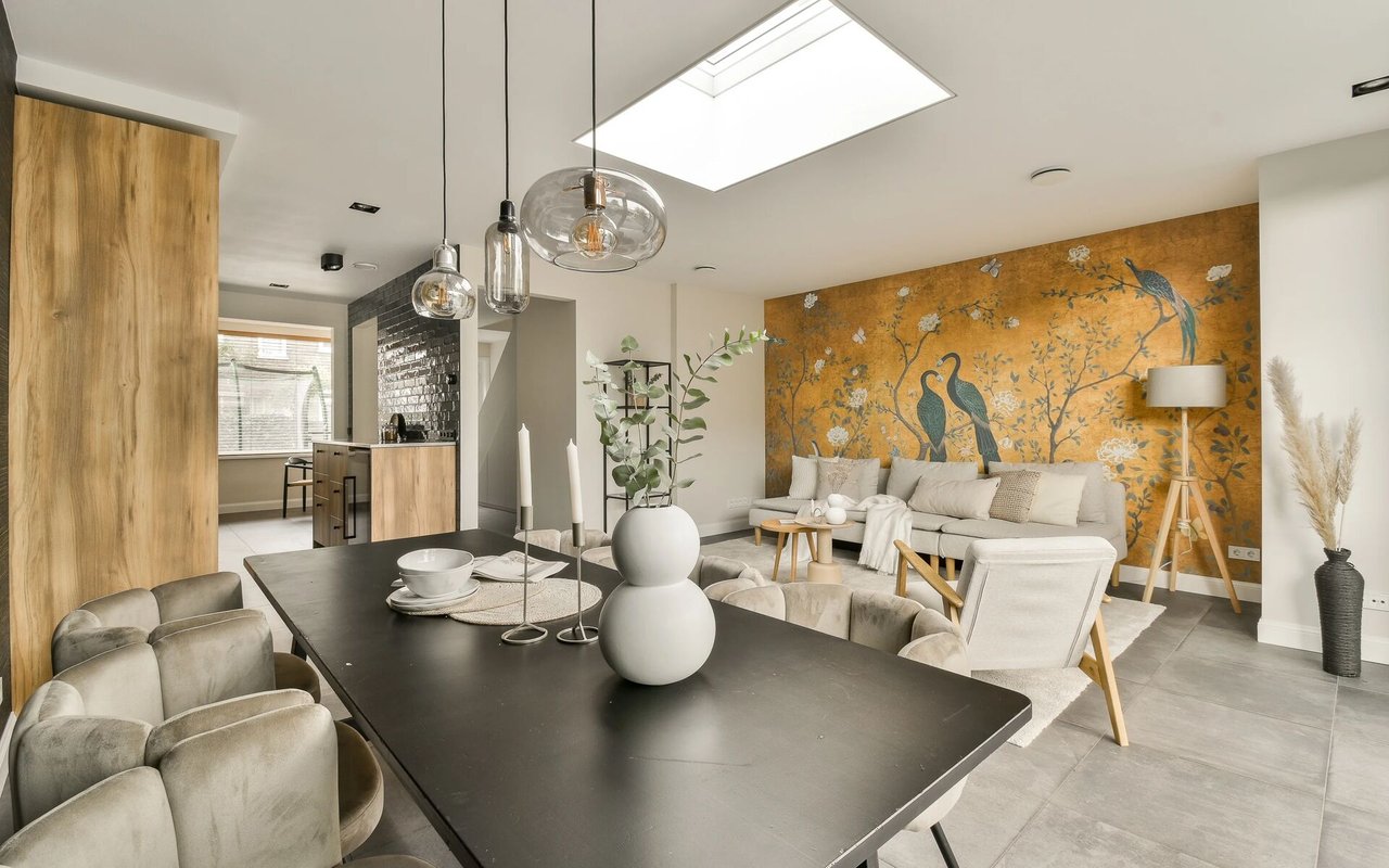 Open-plan living and dining room with mustard bird-patterned wallpaper and a black dining table.