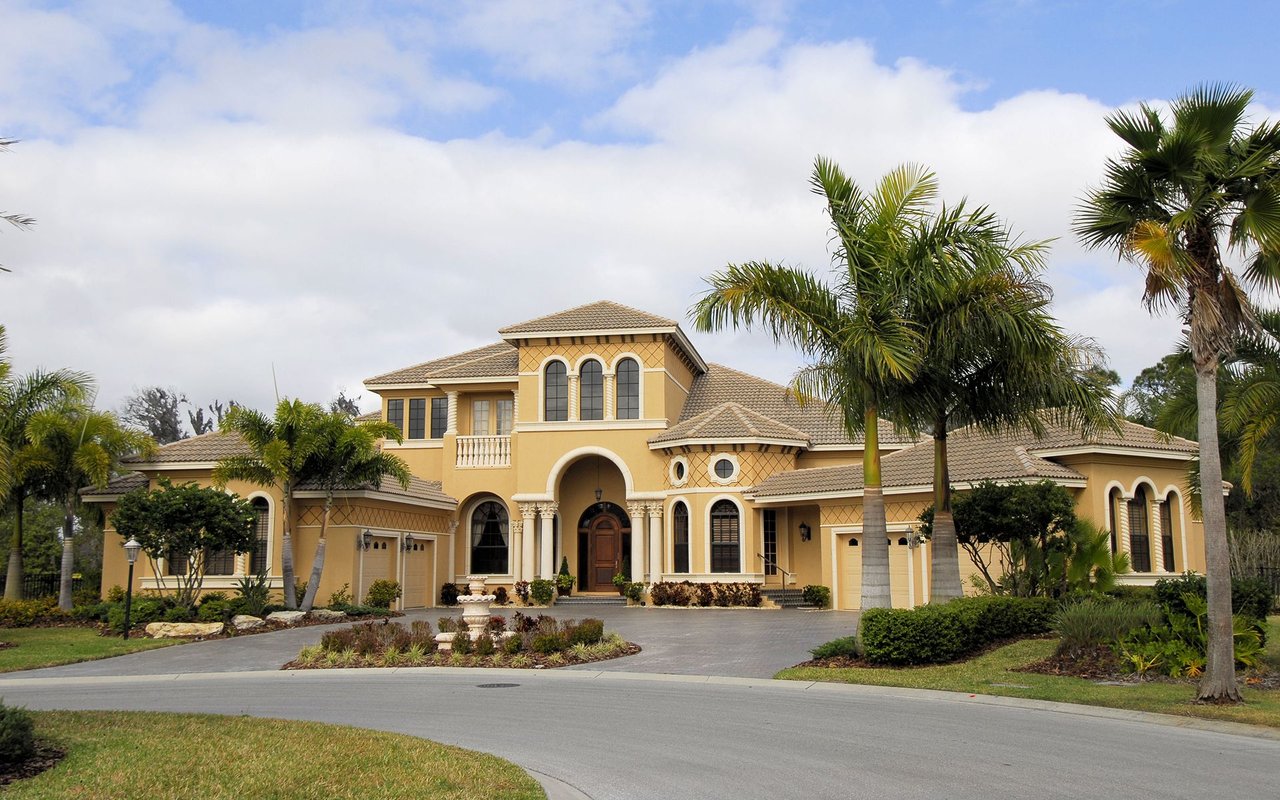 Mediterranean-style home with a tiled roof, arched entrance, palm trees, and landscaped driveway.