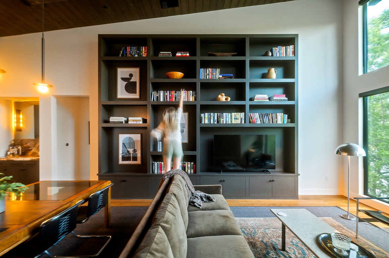 Living and dining spaces along the bookshelf wall over white oak floors, furnished by Liz MacPhail Interiors at 2403 Big Horn Drive, Austin.