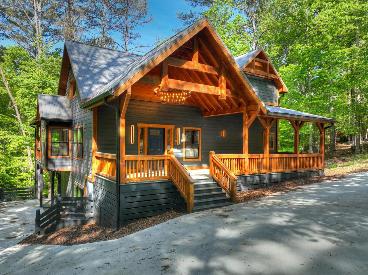 Modern mountain home with timber gables and a broad covered porch in a wooded setting.