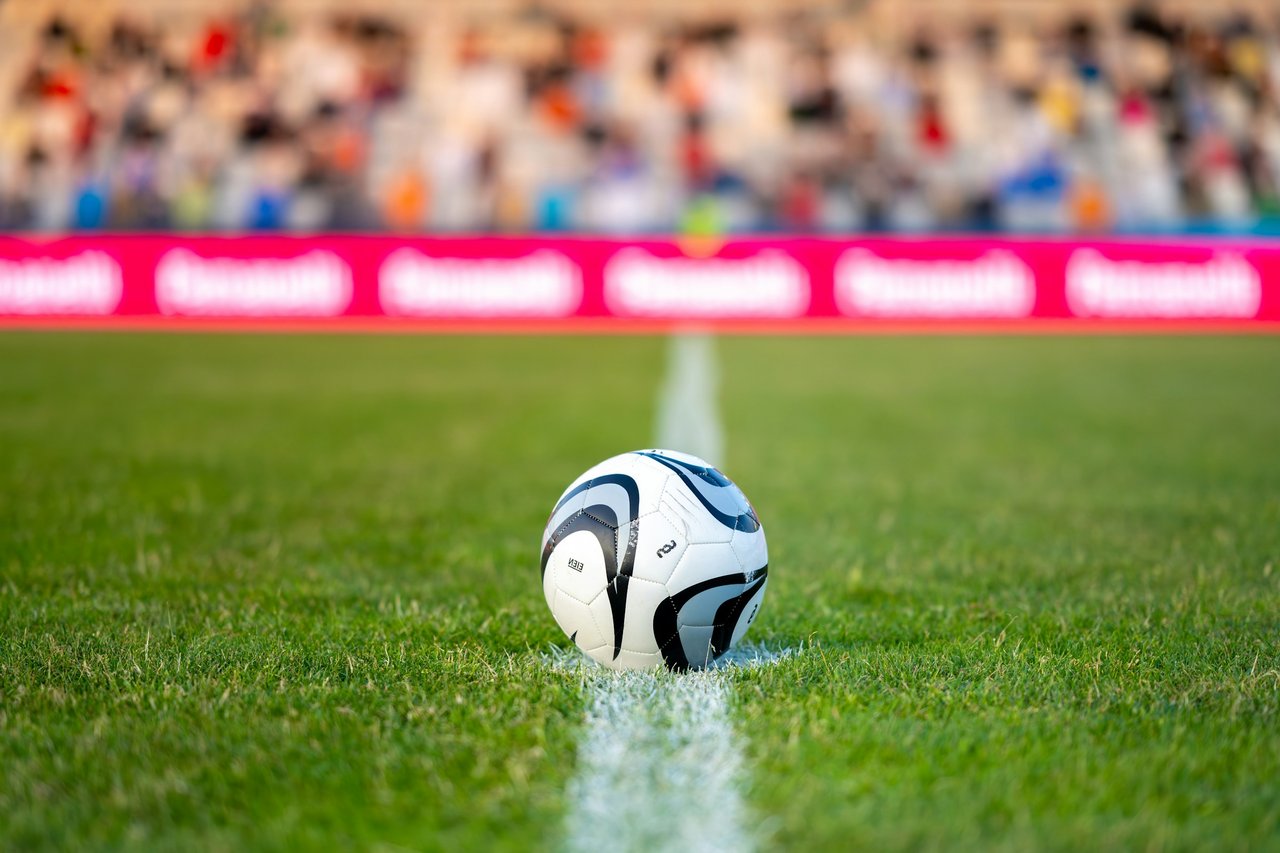 Soccer ball on a field’s center line with a blurred stadium crowd behind it.