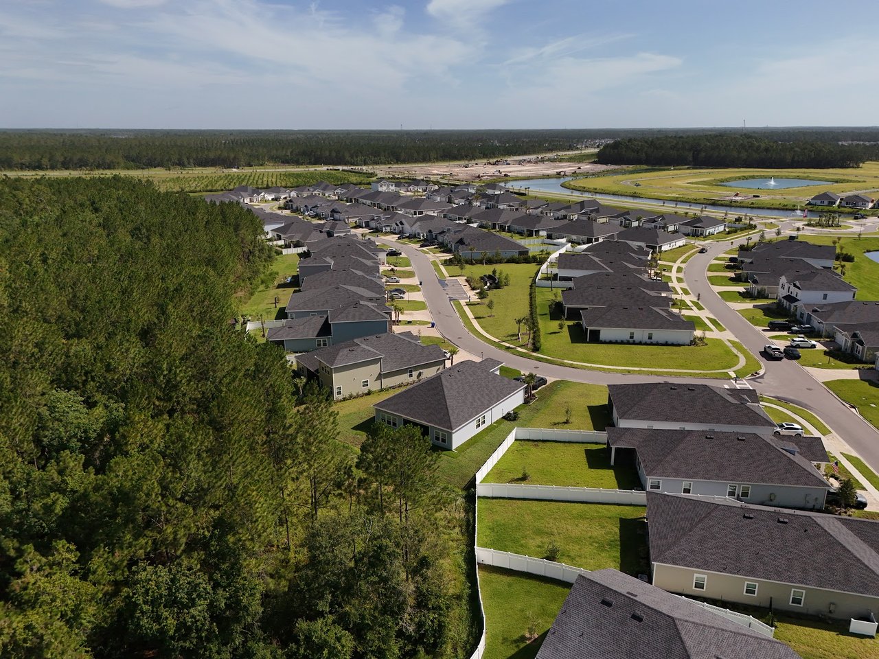 Aerial view of homes along curving streets beside a pond and wooded area.