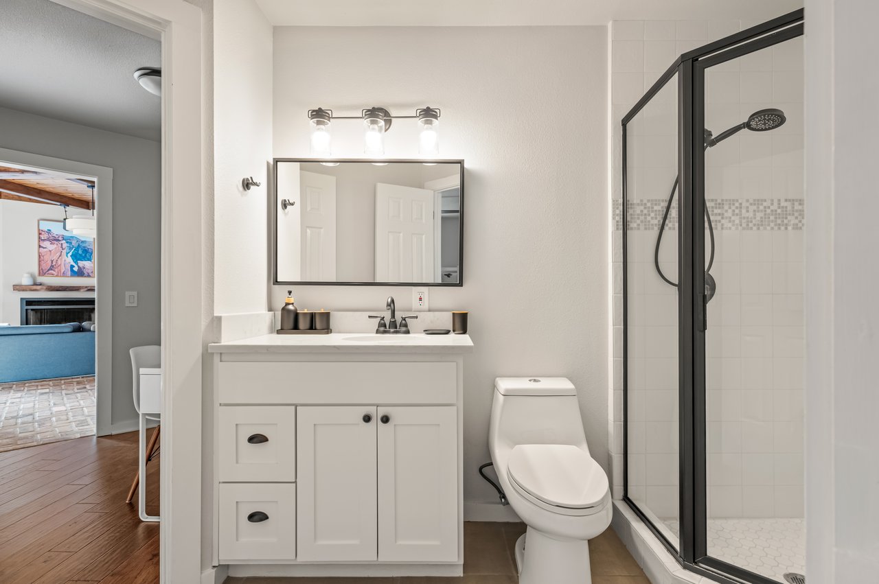 Bathroom with white vanity, wall mirror, toilet, and black-framed glass shower.