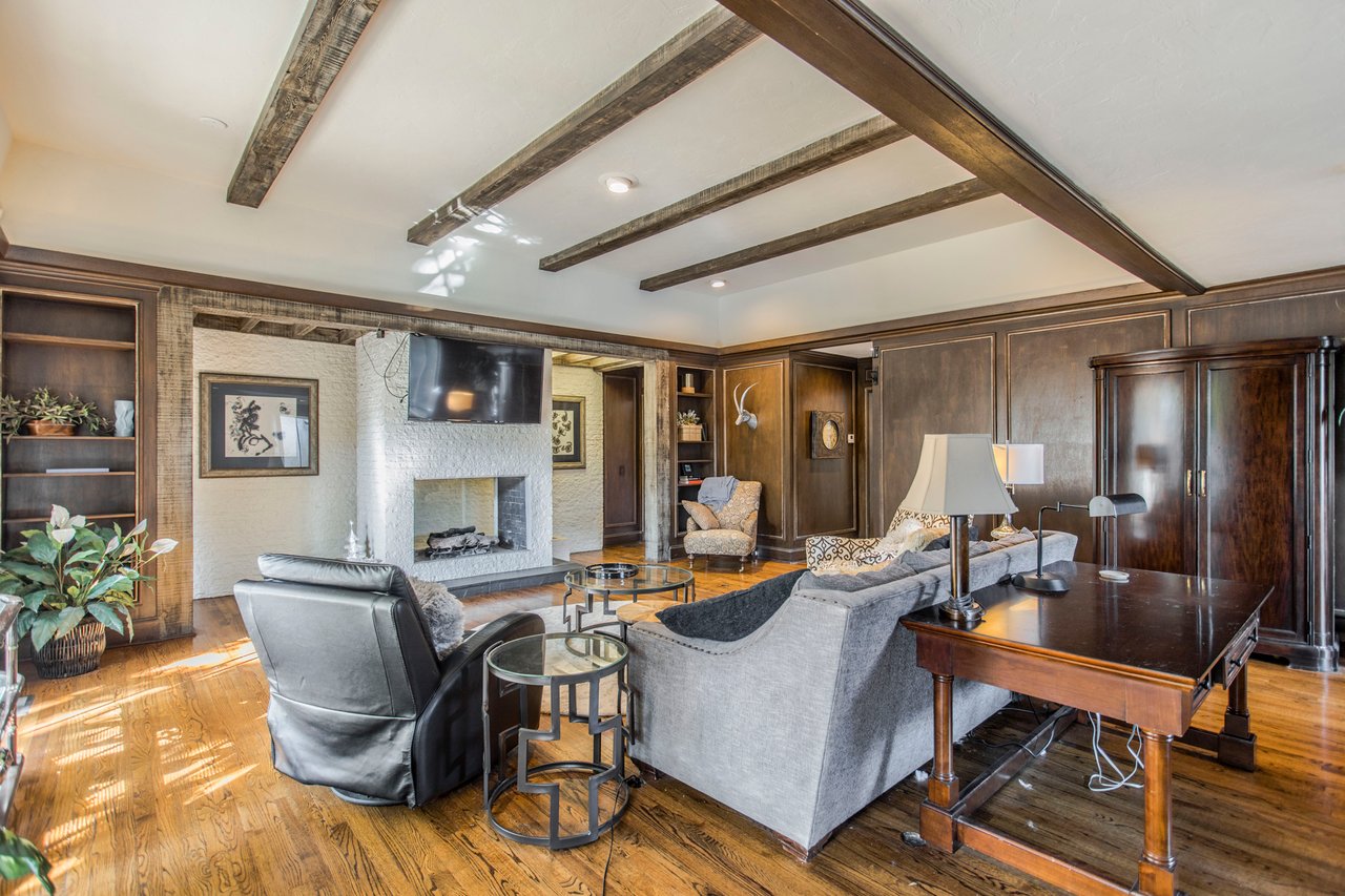 Living room with exposed wood ceiling beams, a white brick fireplace, and hardwood floors.