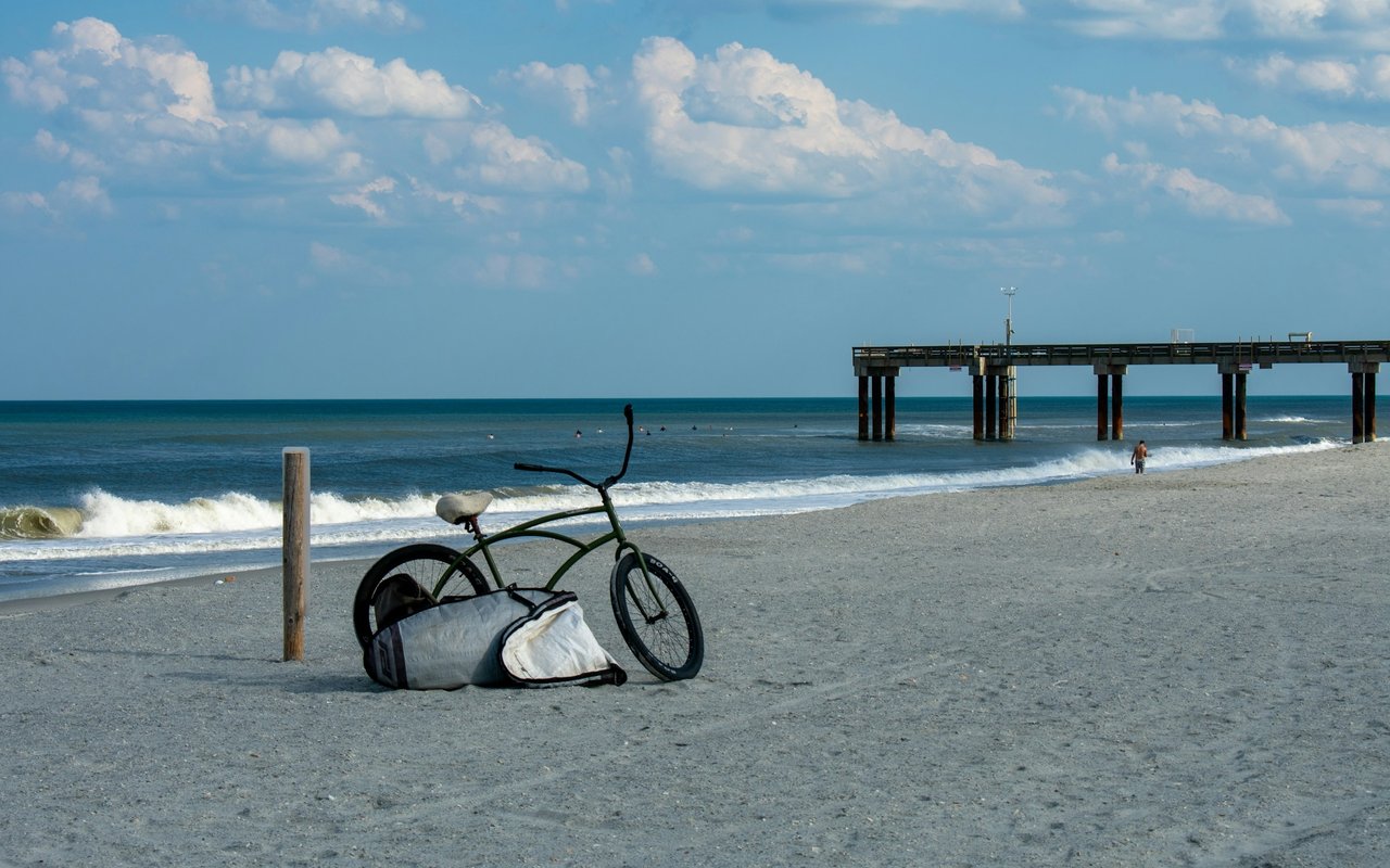 Sandy beach with a fishing pier and a bicycle beside the surf.