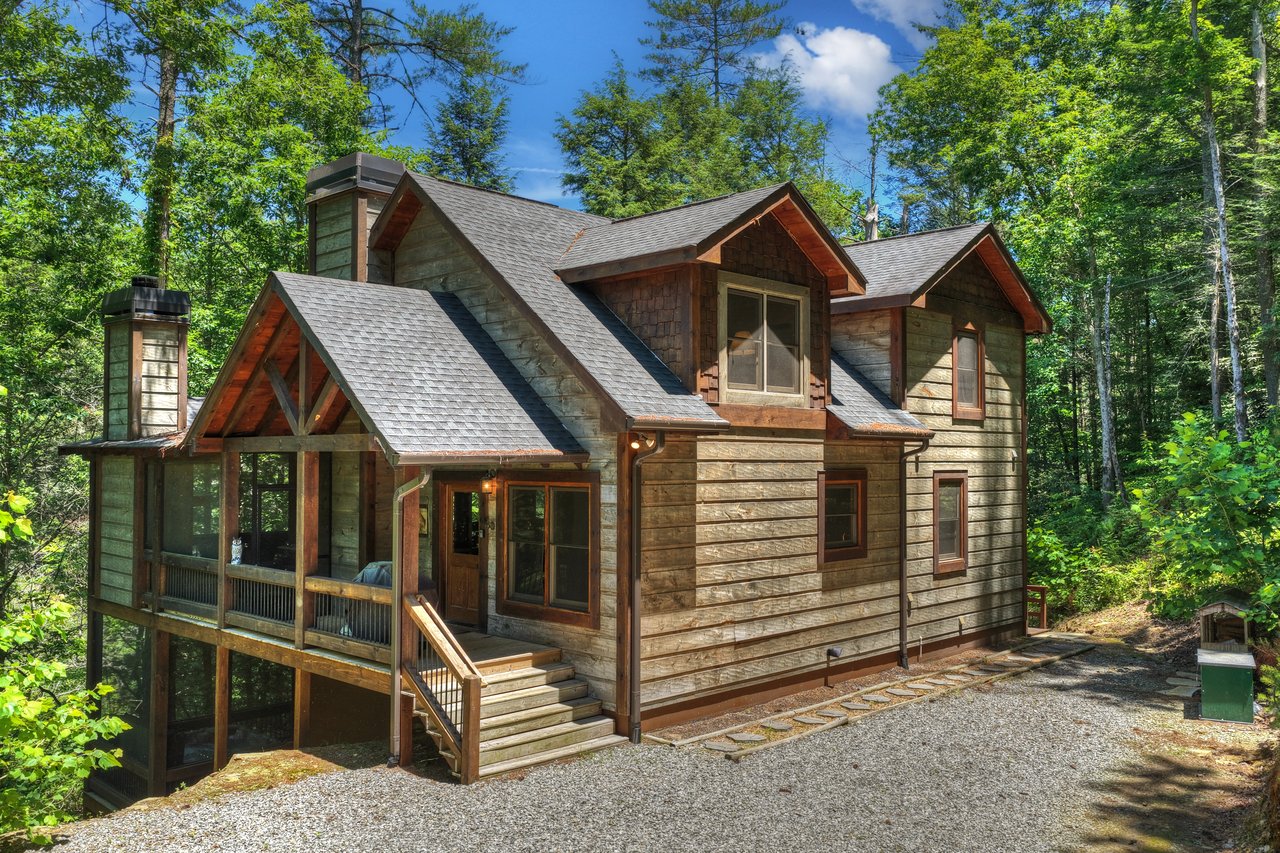 Wood-sided mountain home with a covered porch and gravel driveway in a forest.