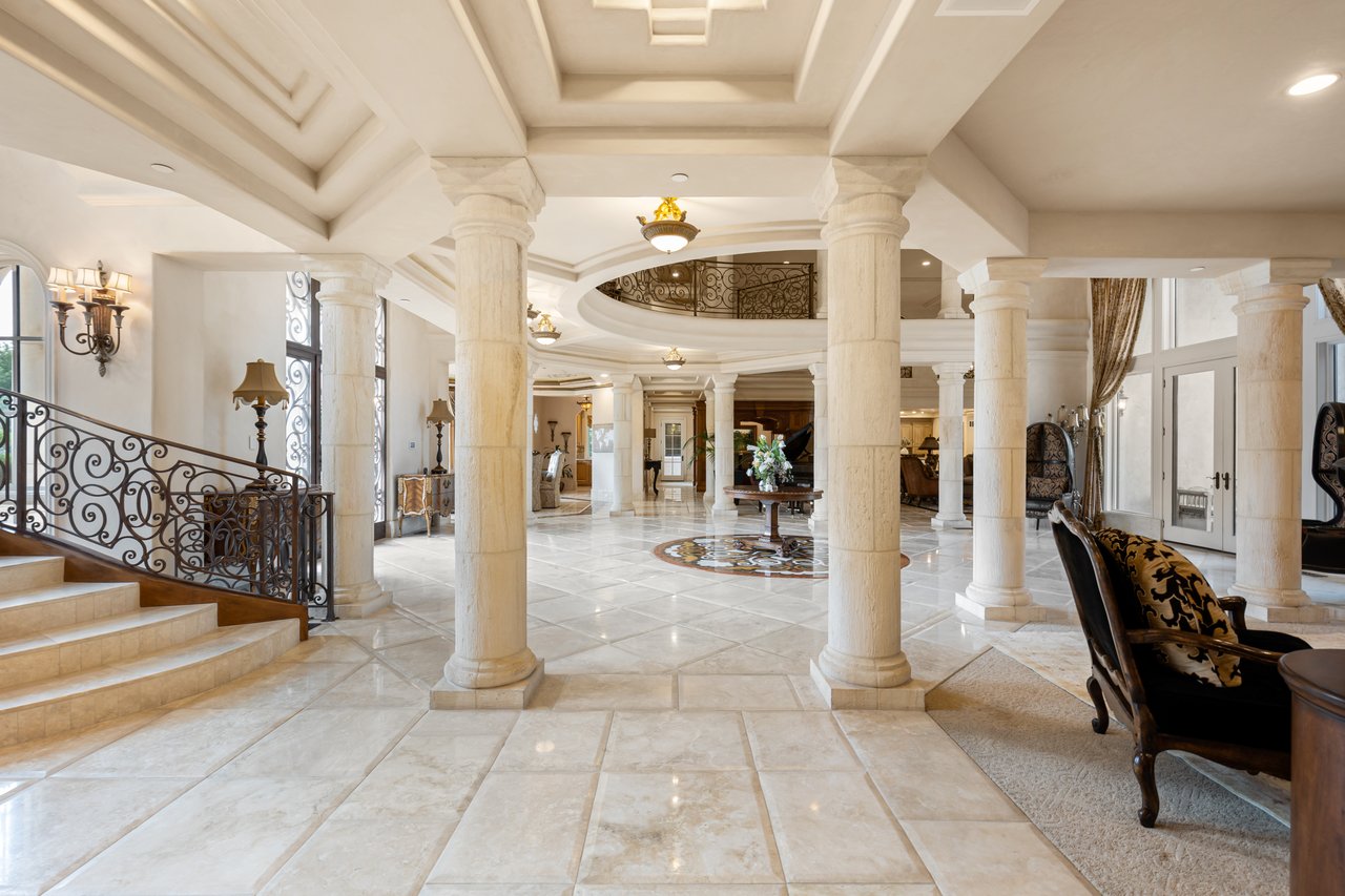Luxury home foyer with marble floors, tall columns, and an ornate staircase and balcony.