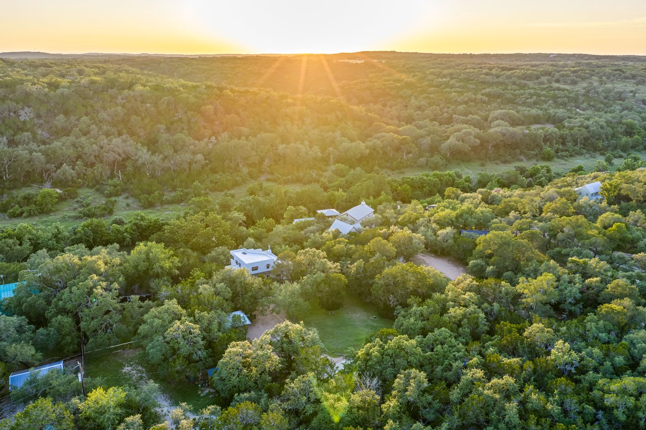 Aerial view of a home among dense trees, with wooded hills glowing in the setting sun.