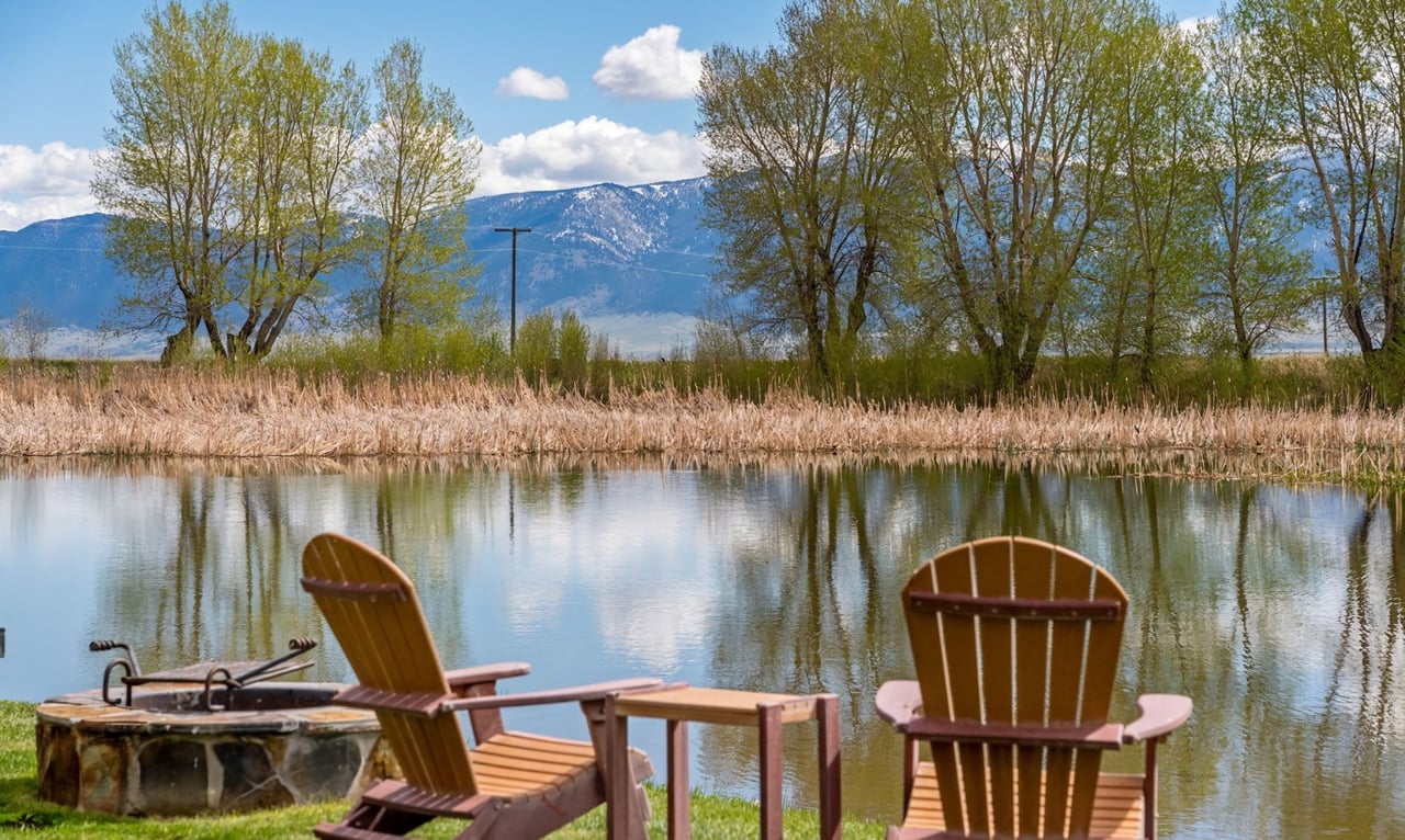 Two wooden Adirondack chairs sit by the edge of a calm lake