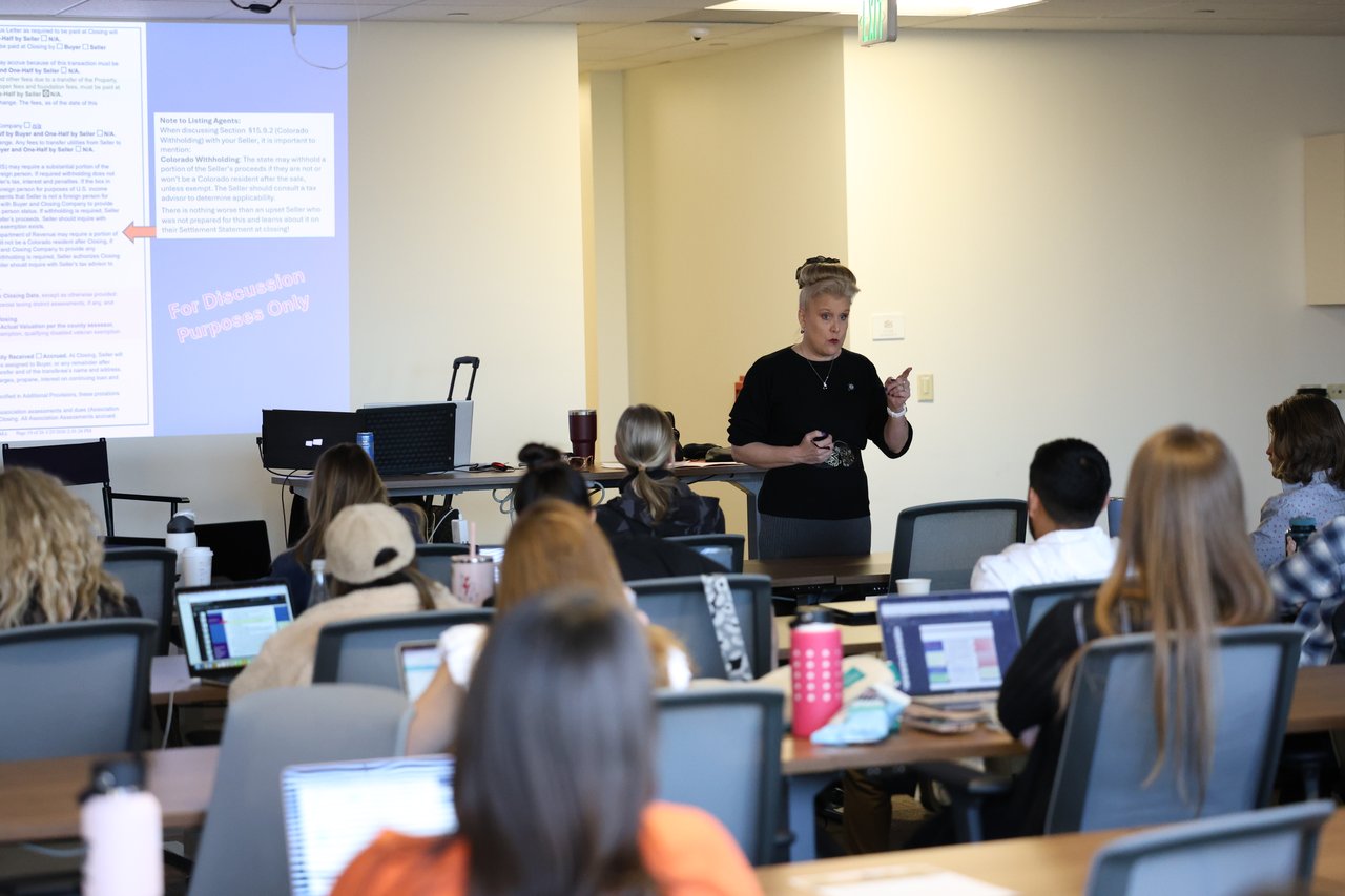 Instructor leads a real estate training session as attendees follow along at laptops.