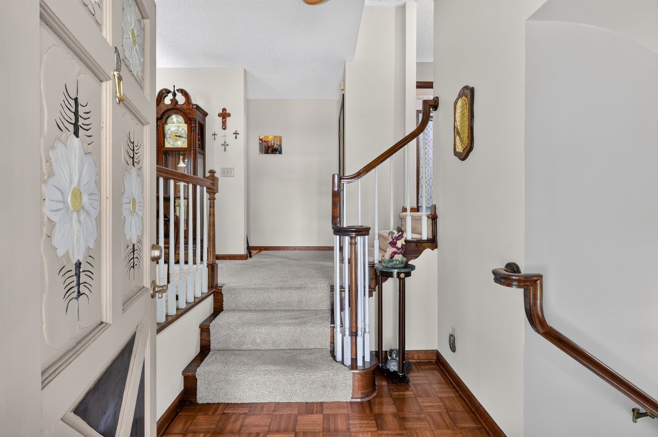 Entry hall with a carpeted staircase, curved wood railings, parquet floor, and grandfather clock.