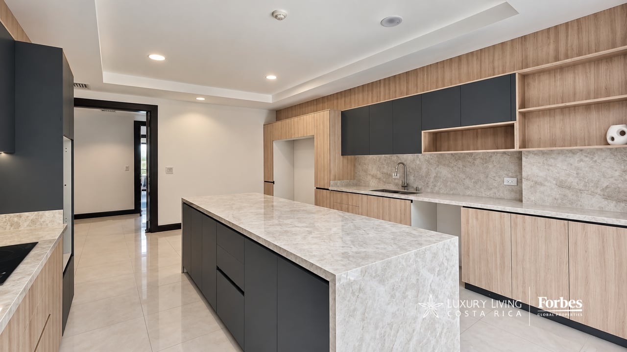 Modern penthouse kitchen with a large stone island, charcoal cabinetry, and light wood shelving.