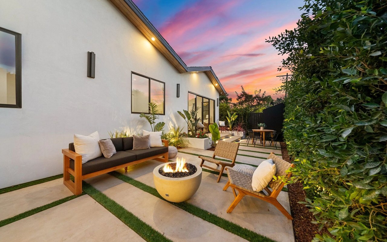 Modern home’s backyard patio with a fire pit, lounge seating, and a colorful sunset sky.