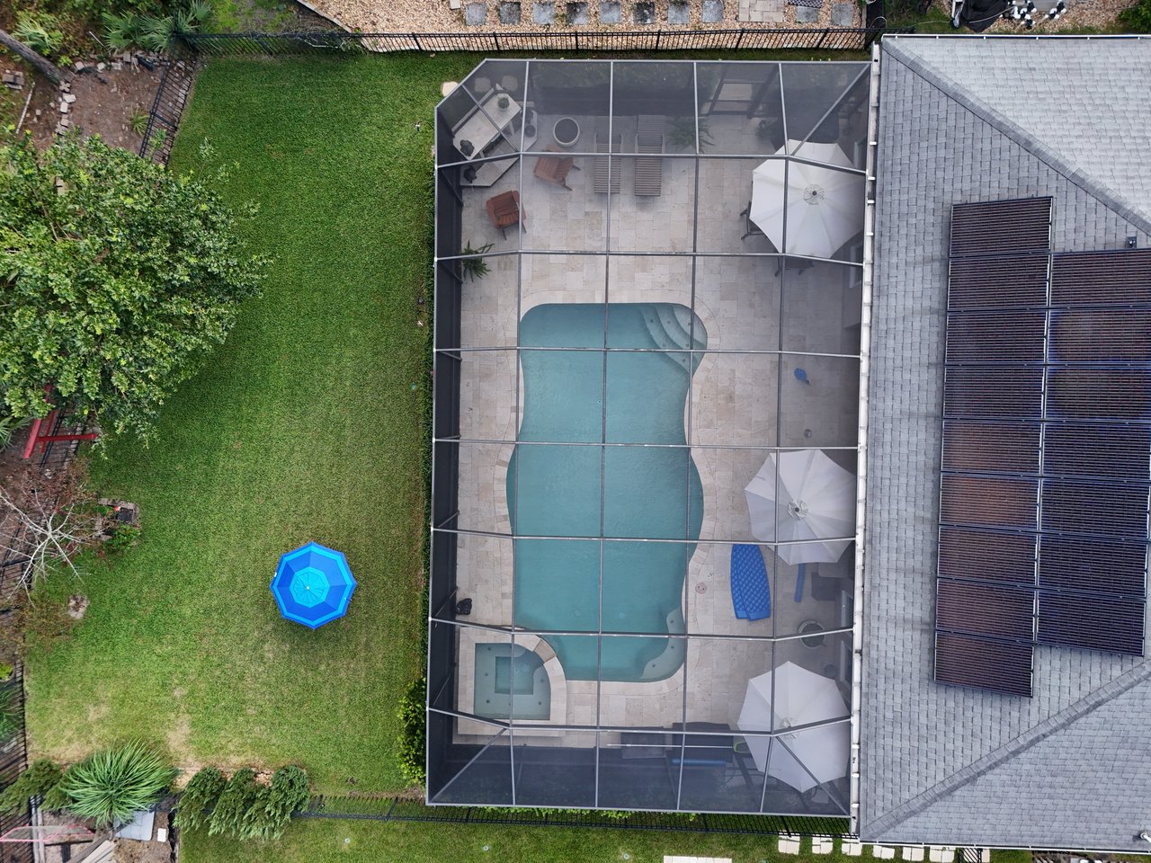 Screened backyard pool with a paved deck, patio furniture, and lawn, viewed from above.