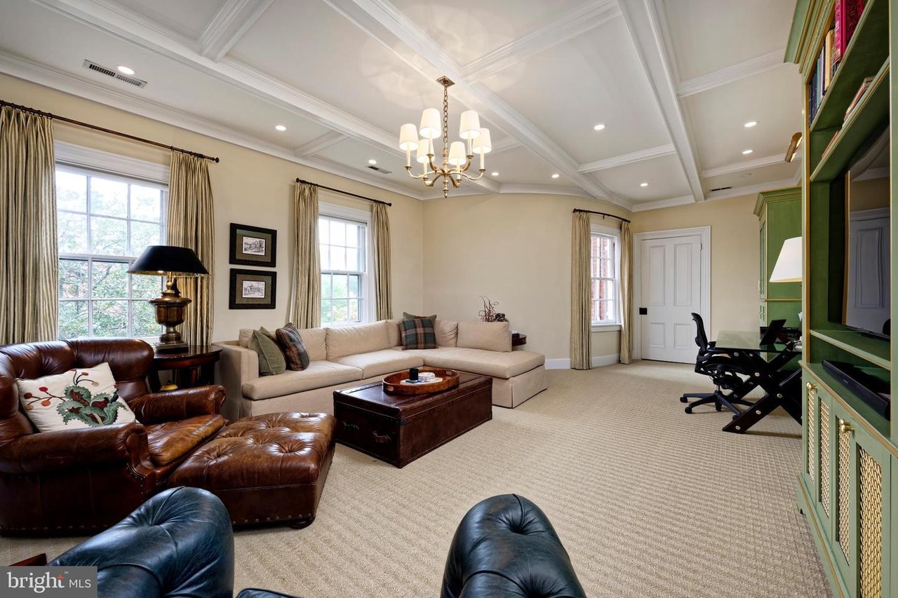 Furnished living room with a coffered ceiling, chandelier, leather armchairs, and green built-in shelving.