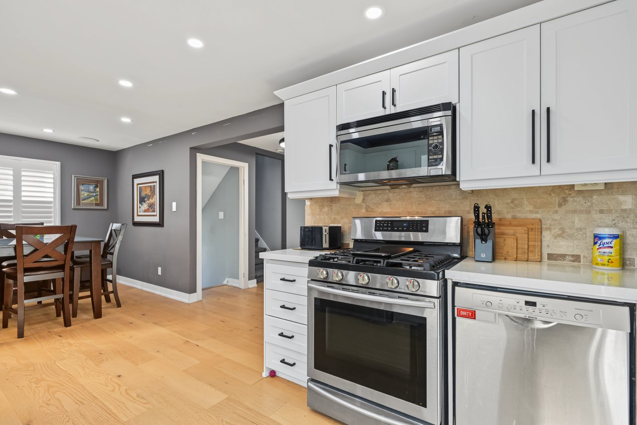 Kitchen with white cabinets, stainless steel appliances, stone backsplash, and an adjoining dining area.
