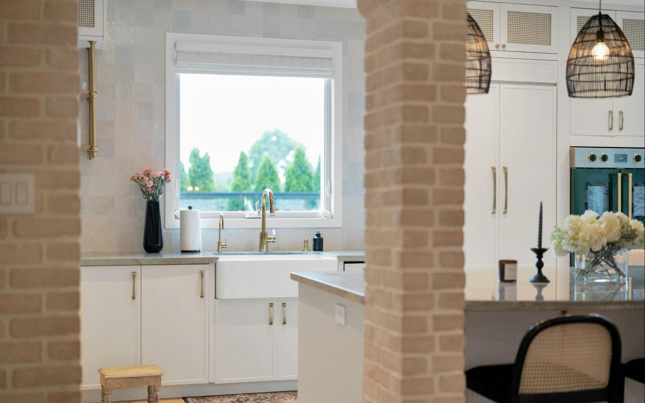 Bright kitchen with white cabinets, farmhouse sink, brass fixtures, and woven pendant lights.