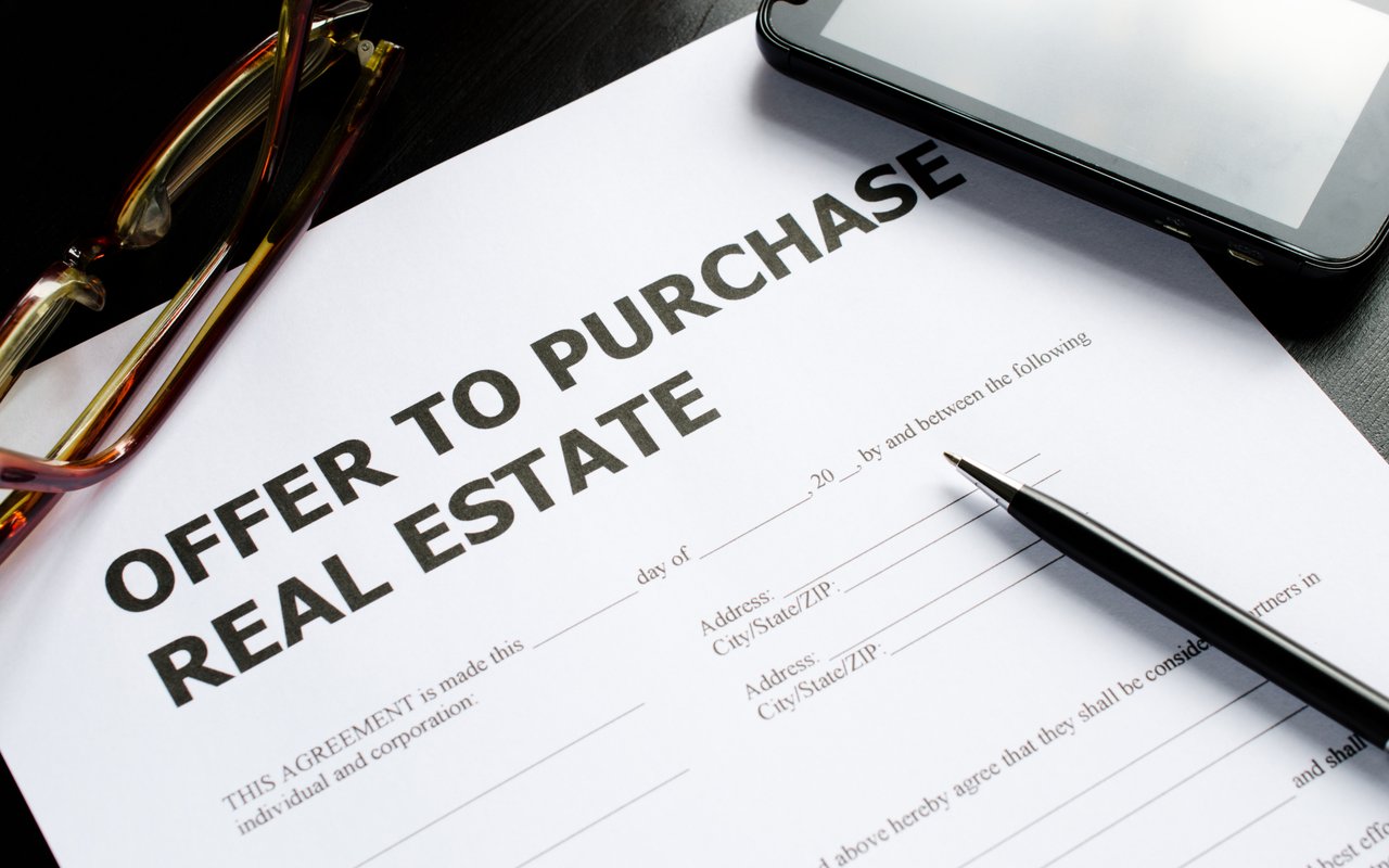 Real estate offer-to-purchase form with eyeglasses, a smartphone, and a pen.