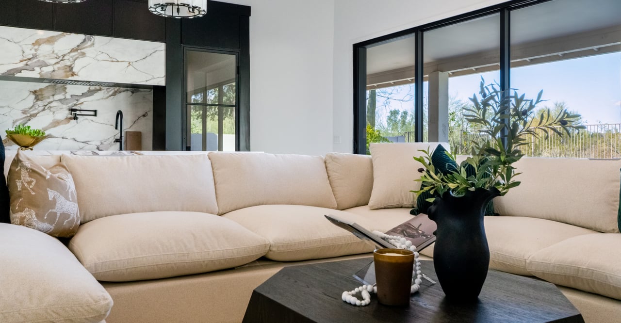 Modern living room with a cream sectional, marble kitchen backsplash, and black-framed glass doors.