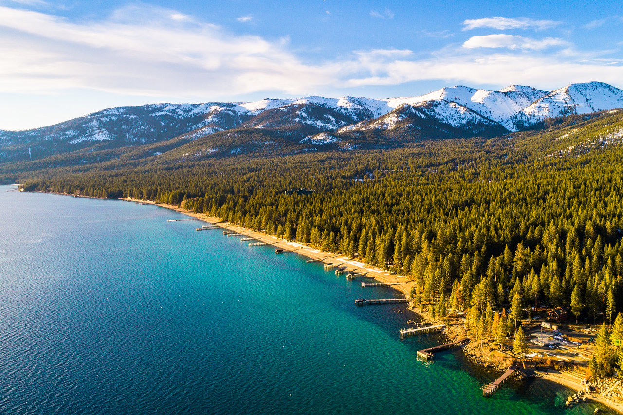 Aerial view of Lakeshore Boulevard in Incline Village Nevada showing private piers and luxury lakefront homes along Lake Tahoe with snow-capped Sierra Nevada mountains