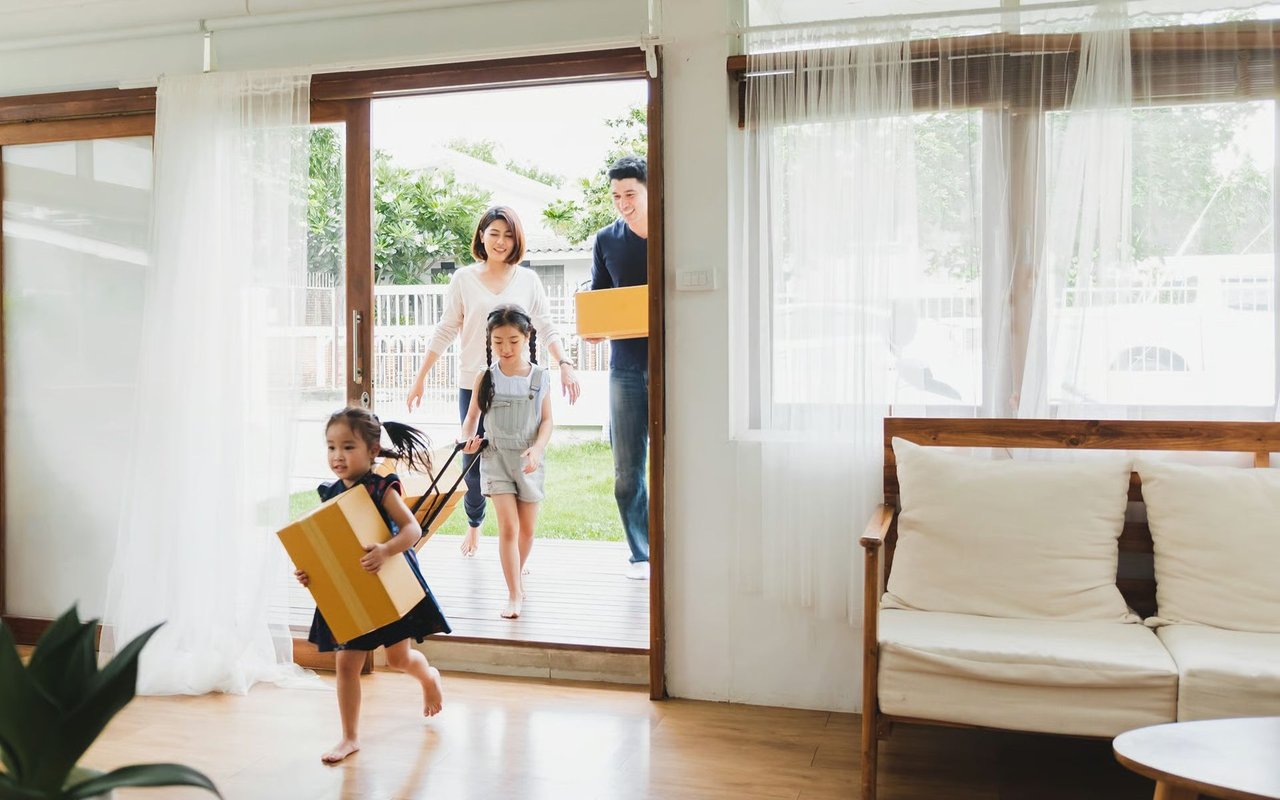 A family carries moving boxes into a bright living room through an open patio doorway.