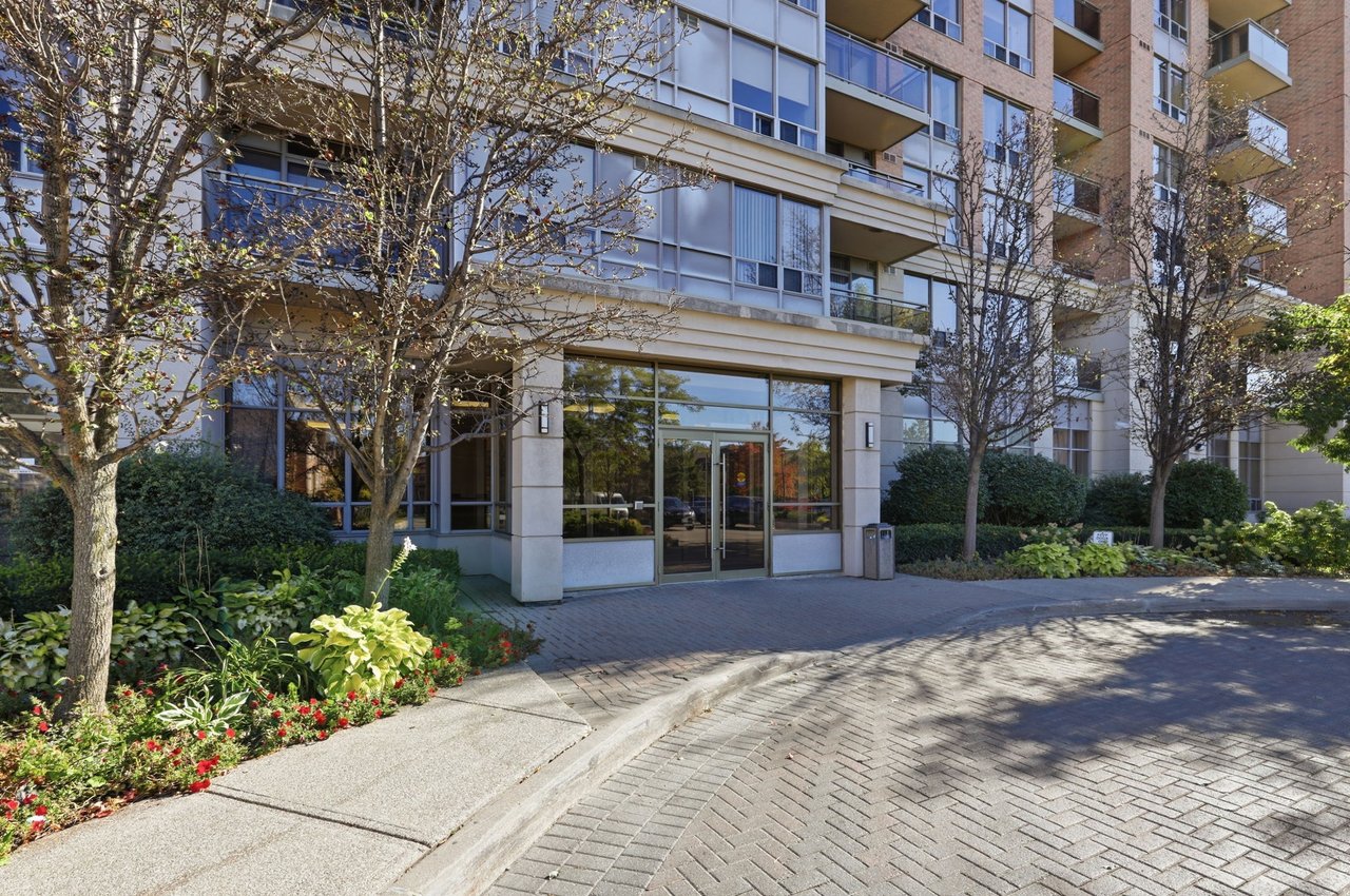 Strathaven condominium entrance framed by landscaped flower beds and trees, with balconies above.