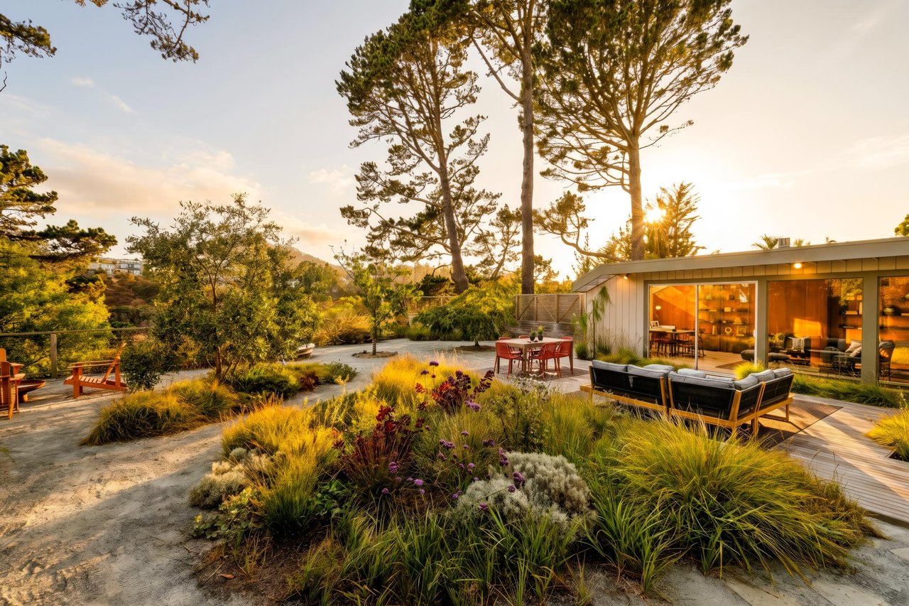 Modern home with a glass-walled living area, outdoor seating, and landscaped garden beneath tall trees.