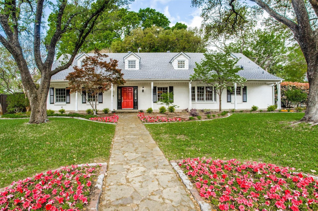 White brick house with a red front door, dormer windows, and flower-lined stone walkway.