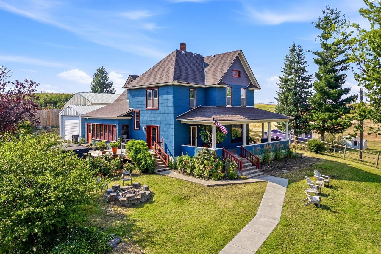 Blue two-story house with a covered porch, detached garage, and landscaped yard with a fire pit.