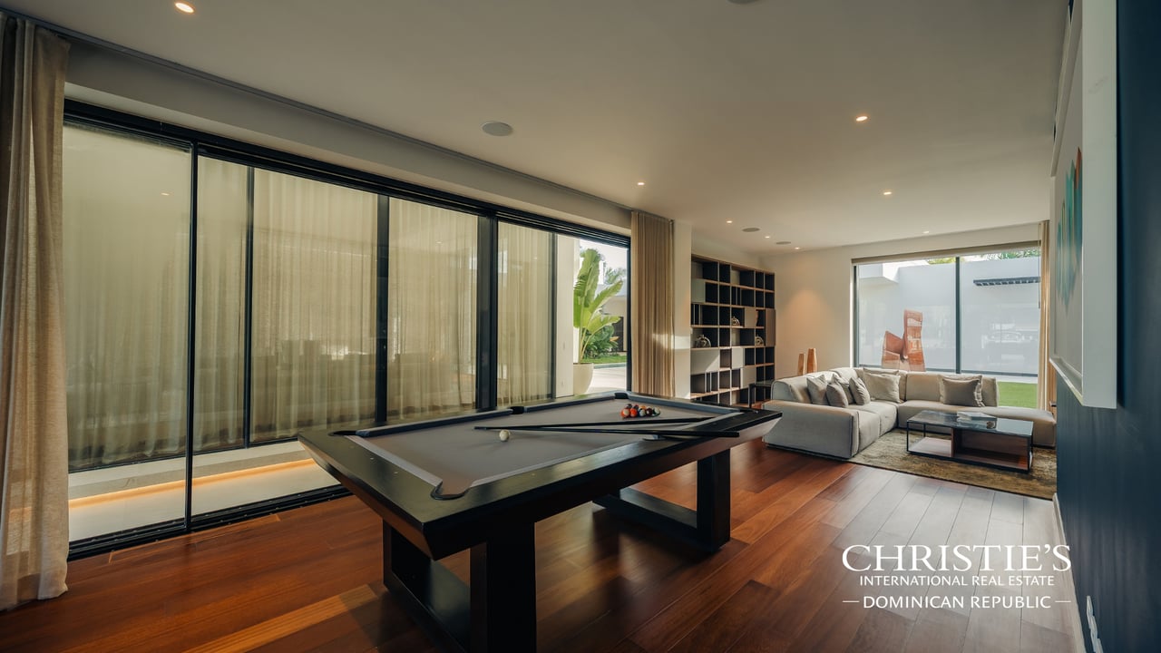 Villa game room with a black pool table, gray sectional sofa, and floor-to-ceiling glass doors.