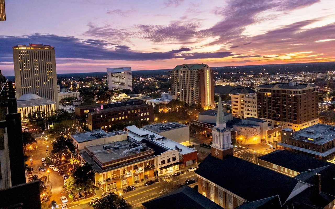 Downtown Tallahassee buildings and church steeple beneath a colorful dusk sky.