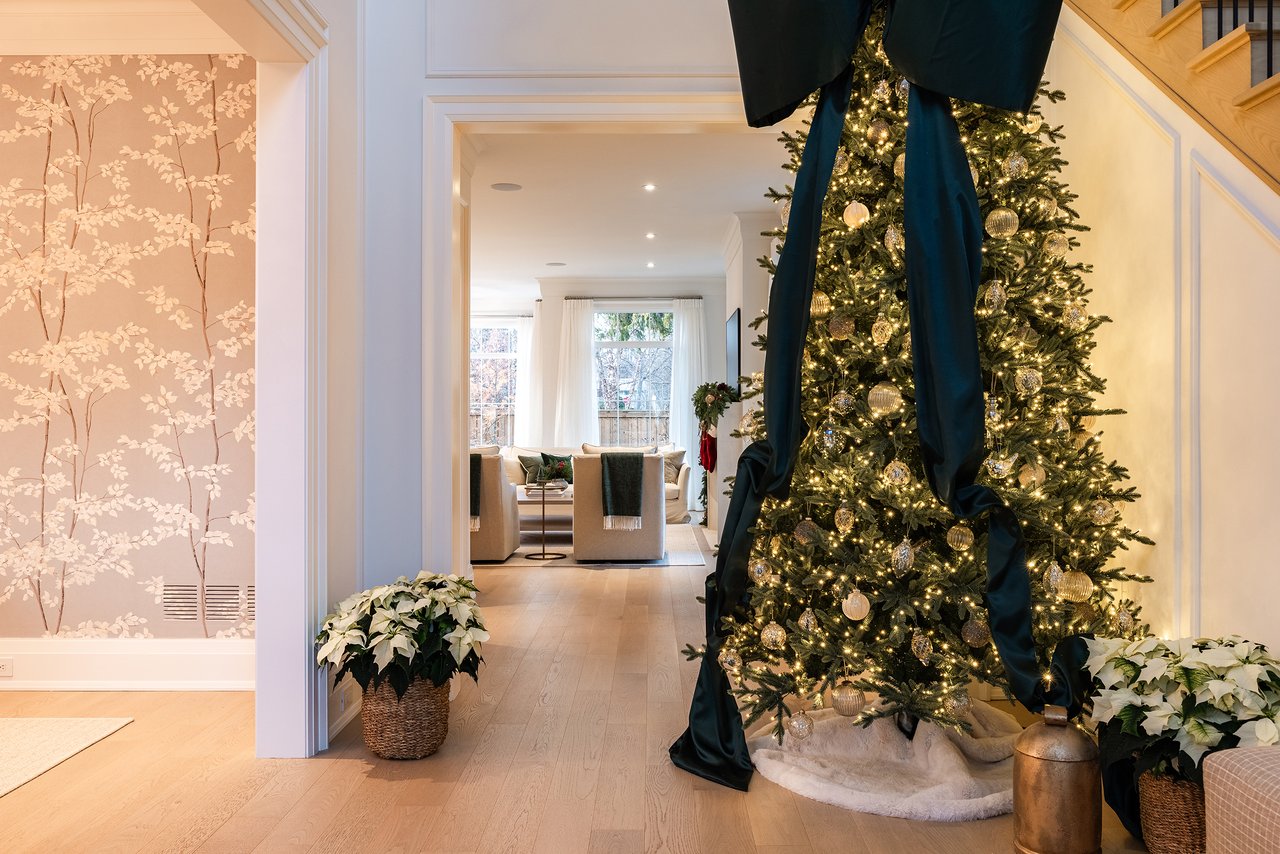 Holiday tree in an Oakville custom home with a view into the living room featuring neutral furniture and seasonal greenery.