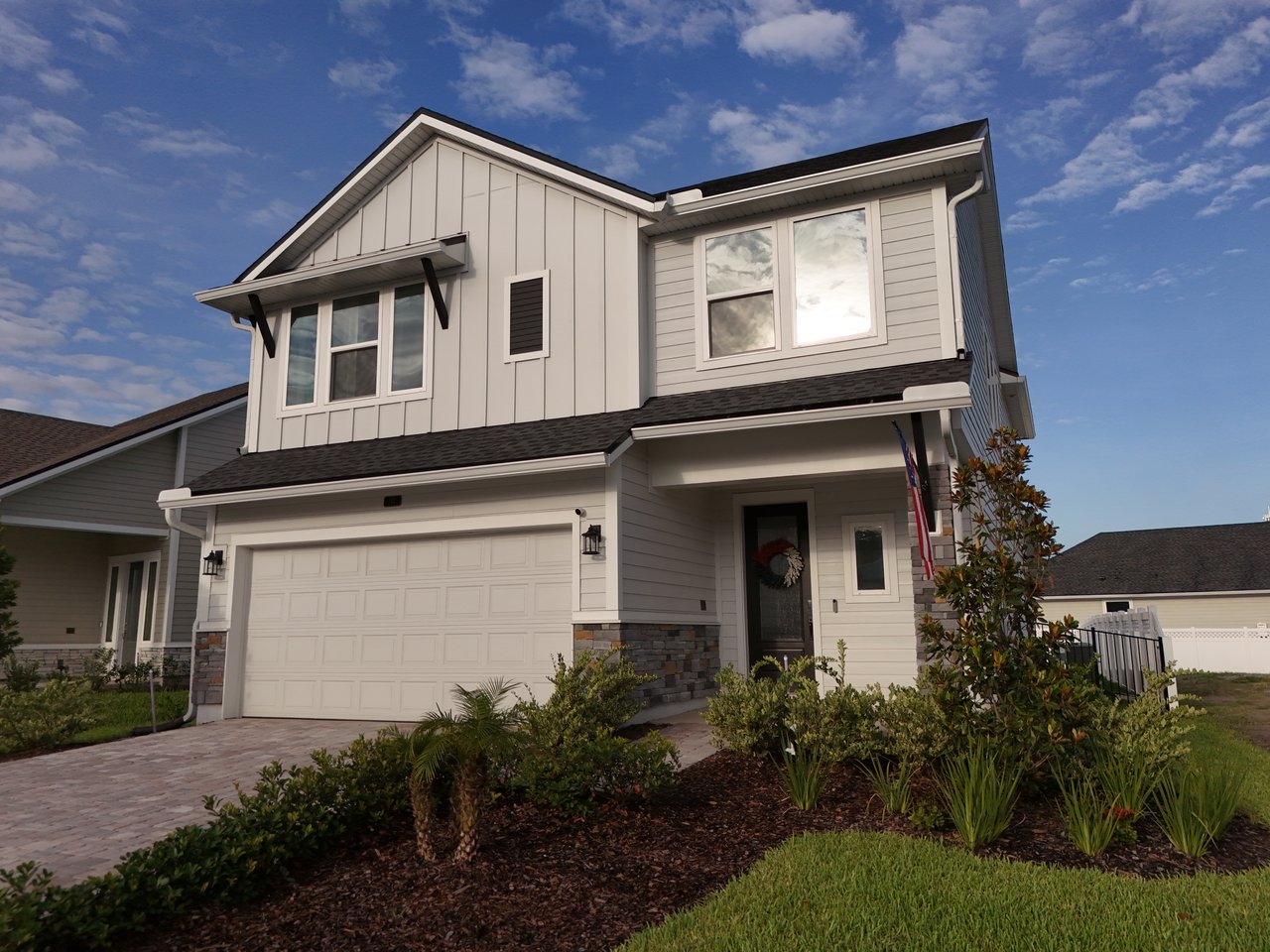 Two-story light-gray home with a double garage, covered entry, and landscaped front yard.
