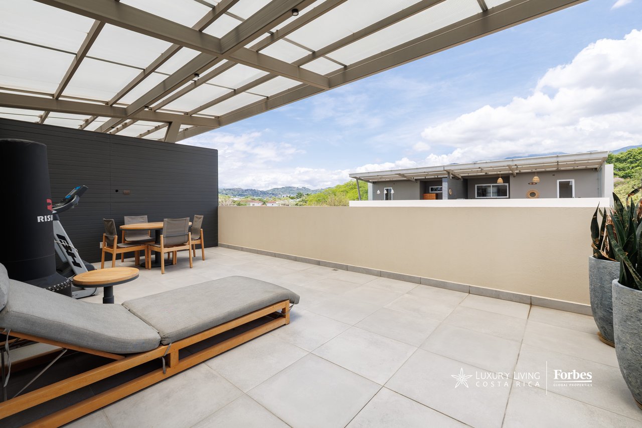 Rooftop terrace with pergola, lounge chairs, dining set, and distant hills.
