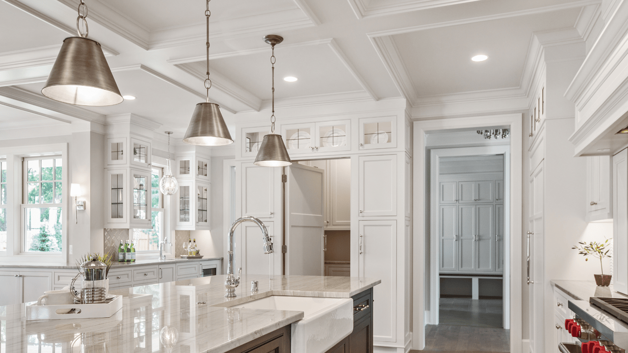 Luxury kitchen with a marble island, apron-front sink, white cabinetry, and metal pendant lights.