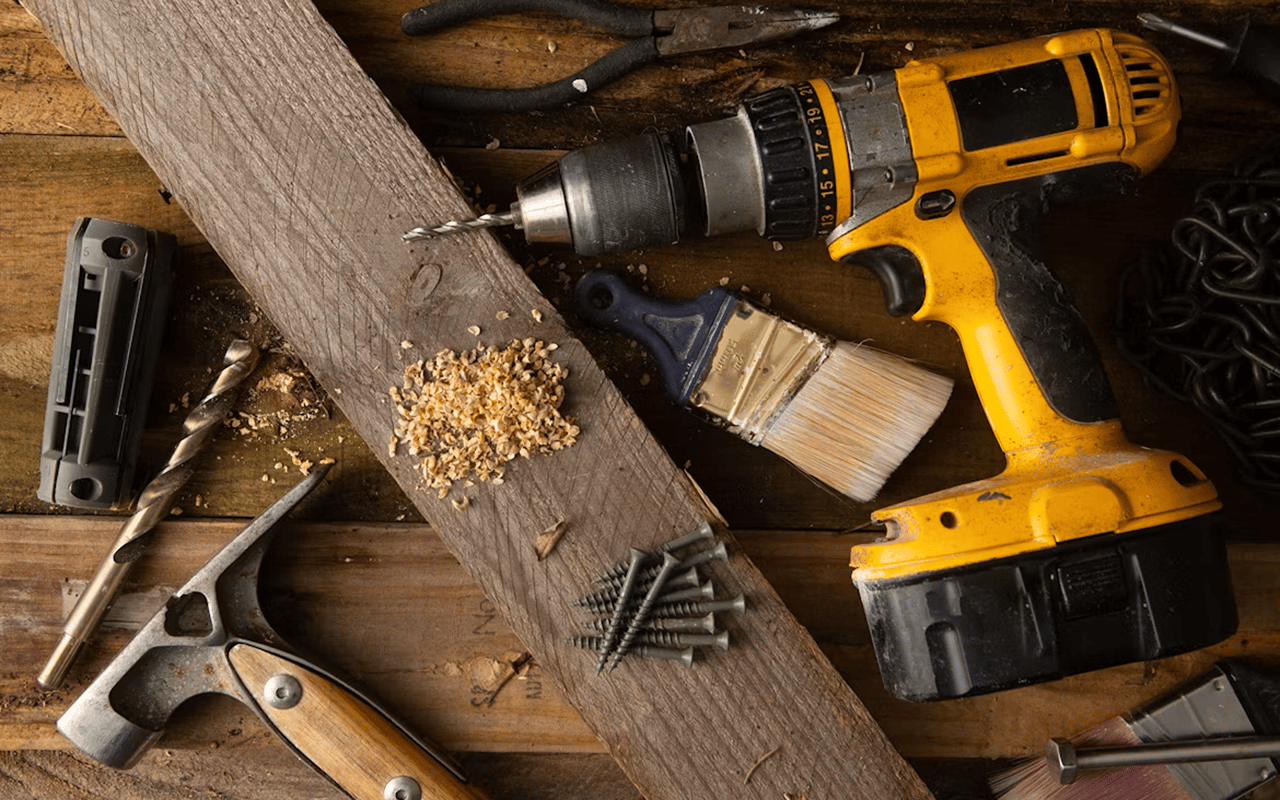 Cordless drill and other woodworking tools arranged on a weathered workbench.