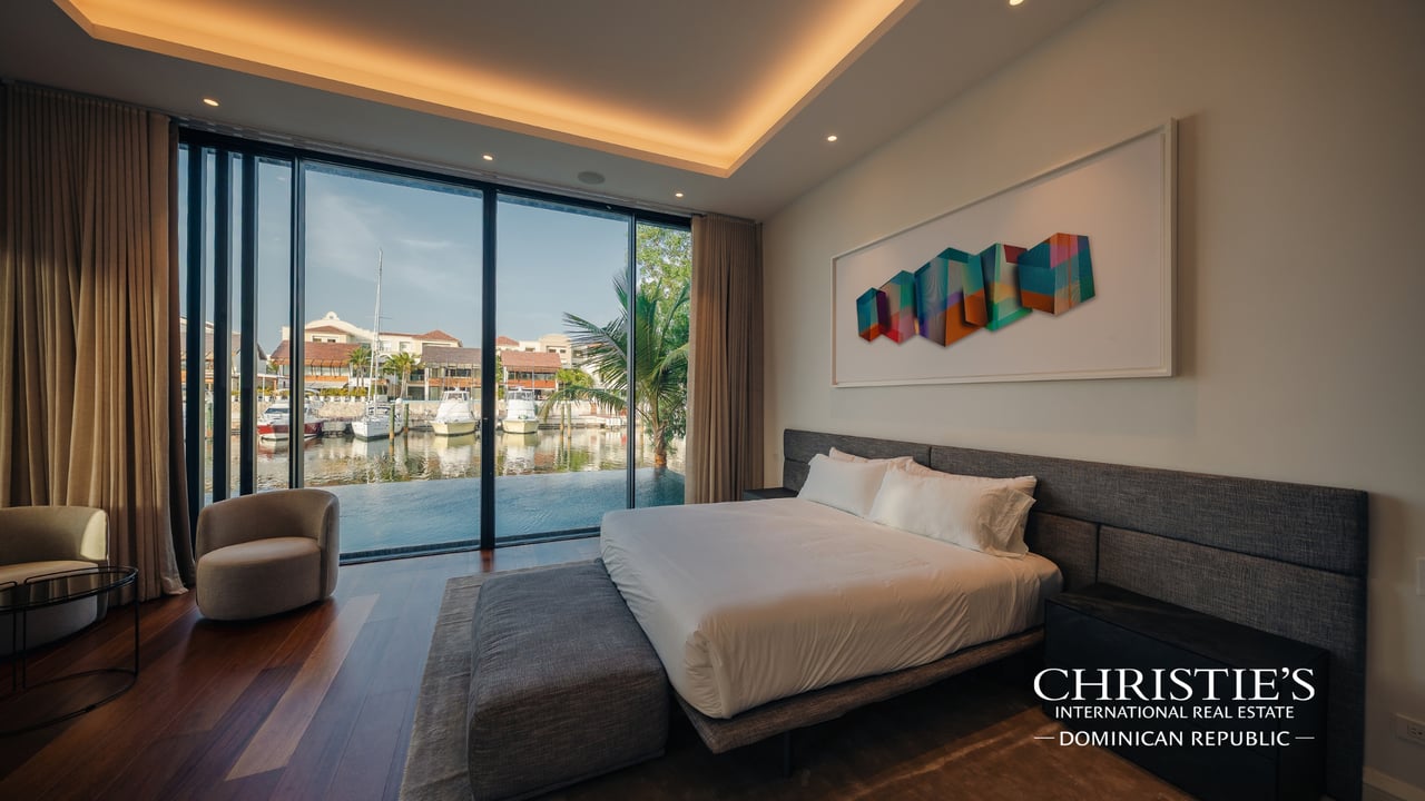 Modern bedroom with a king-size bed and floor-to-ceiling windows overlooking a marina.