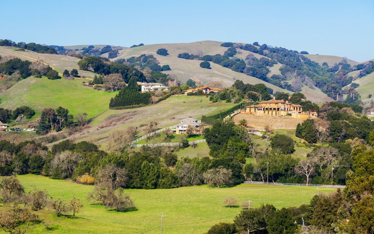Estate homes among rolling green hills, with white fences and tree-lined grounds.