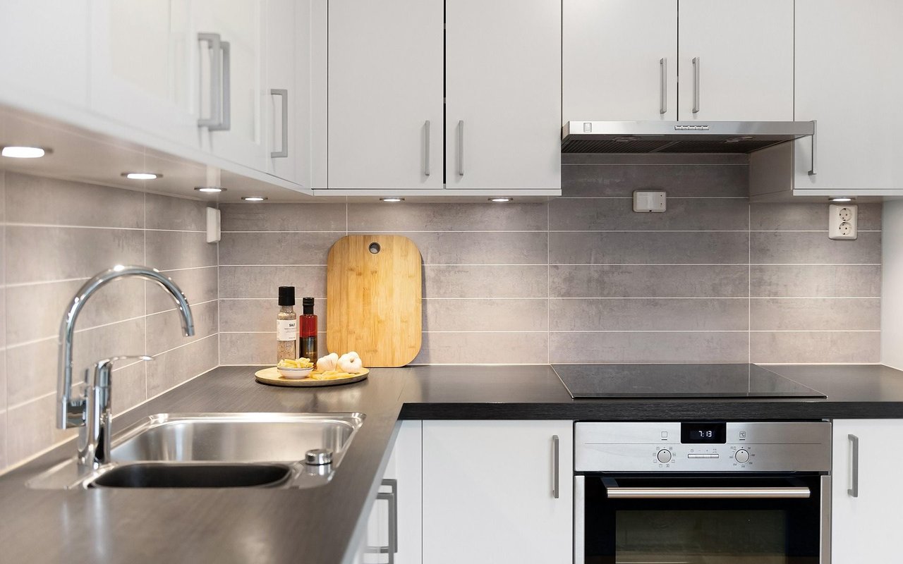 Modern kitchen with white cabinets, gray tile backsplash, dark countertops, and stainless steel appliances.