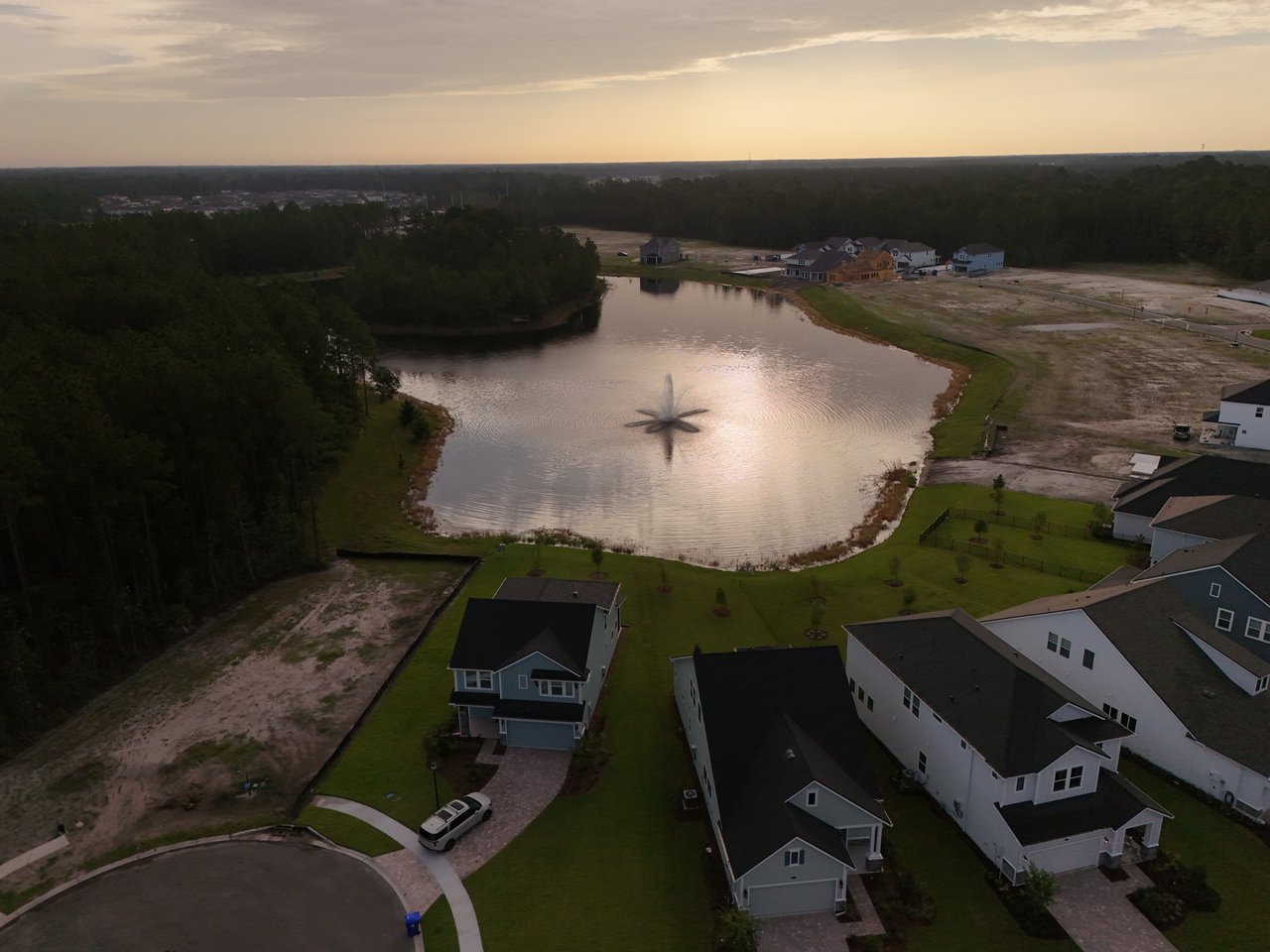 Aerial view of homes around a lake, with wooded areas and construction lots nearby.