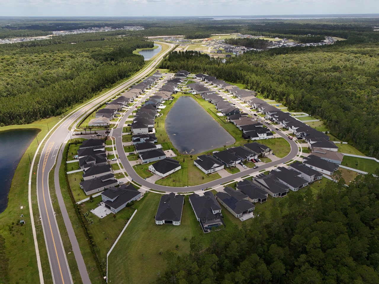 Aerial view of a neighborhood with homes arranged around a pond and woodland.