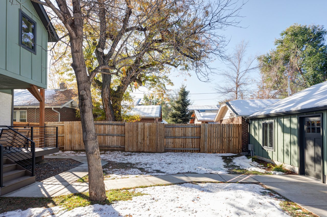 Backyard with mature tree in the middle, a paved path leading between home and garage, bordered by a wooden fence