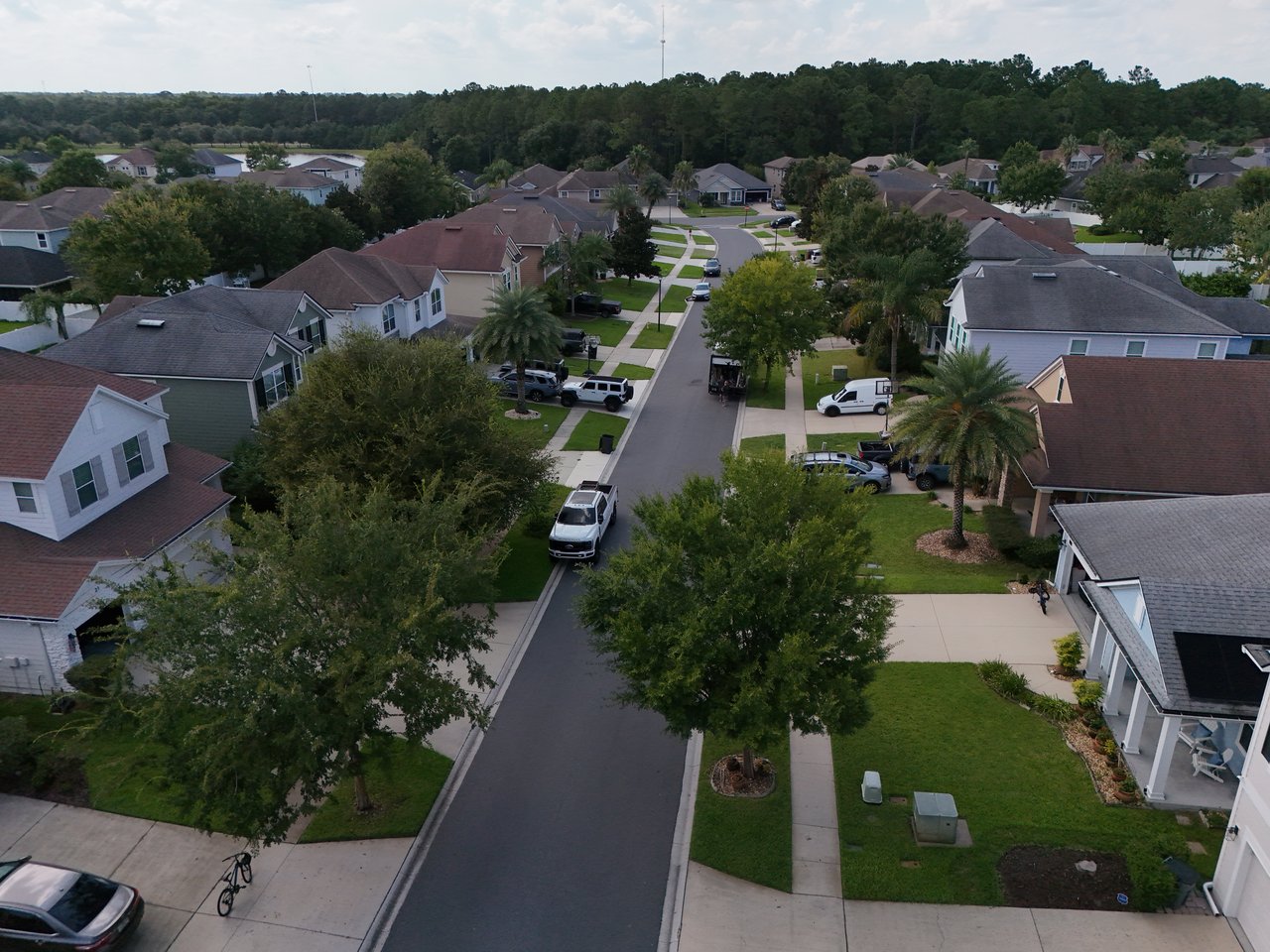 Aerial view down a tree-lined residential street in Greenleaf Village, with homes and parked vehicles.