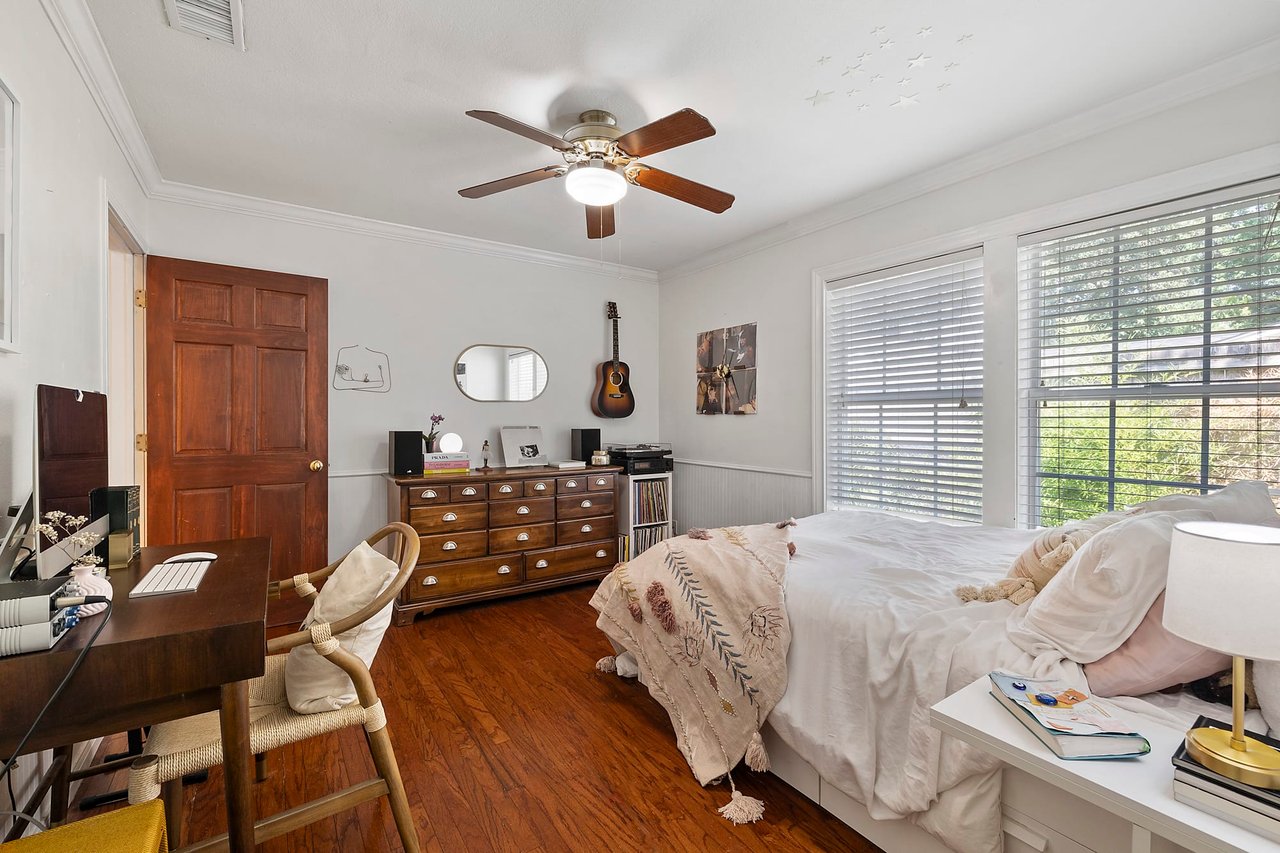 Guest bedroom with original wood floors, a desk nook, and a brass bed at this Tarrytown, Austin home.