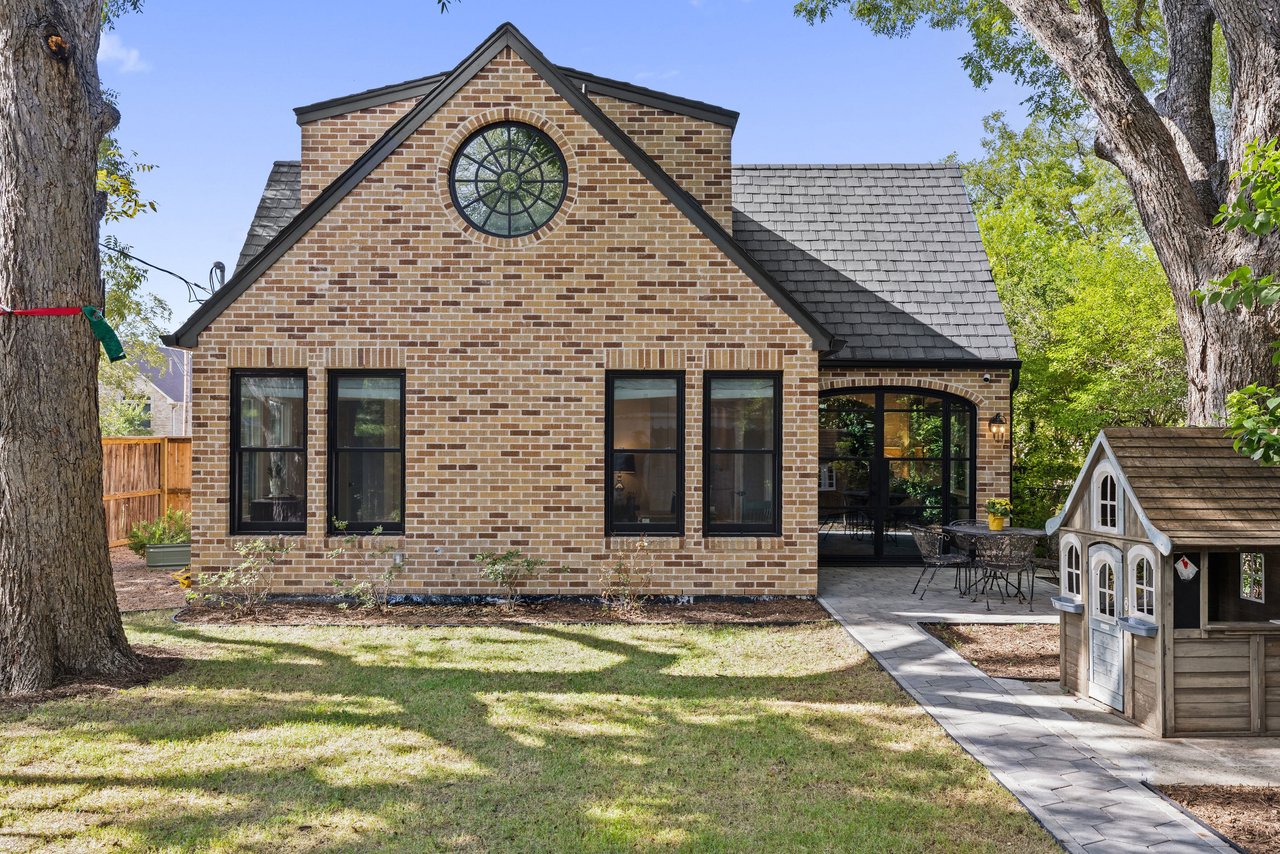 Brick house with a round gable window, glass-enclosed patio, and small playhouse in the yard.